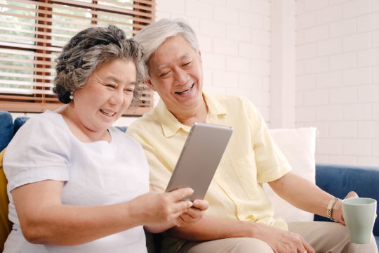 Asian elderly couple using tablet and drinking coffee in living